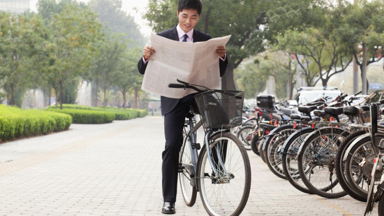 Man on bike reading a newspaper