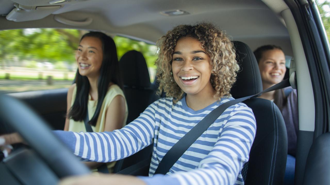 Young girl driving car with friends in passenger and back seats