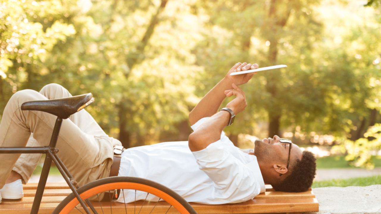 Content man on a bench next to a bike reading a newspaper.