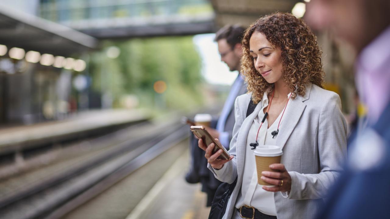 Woman waiting at a rail station reading a newspaper.