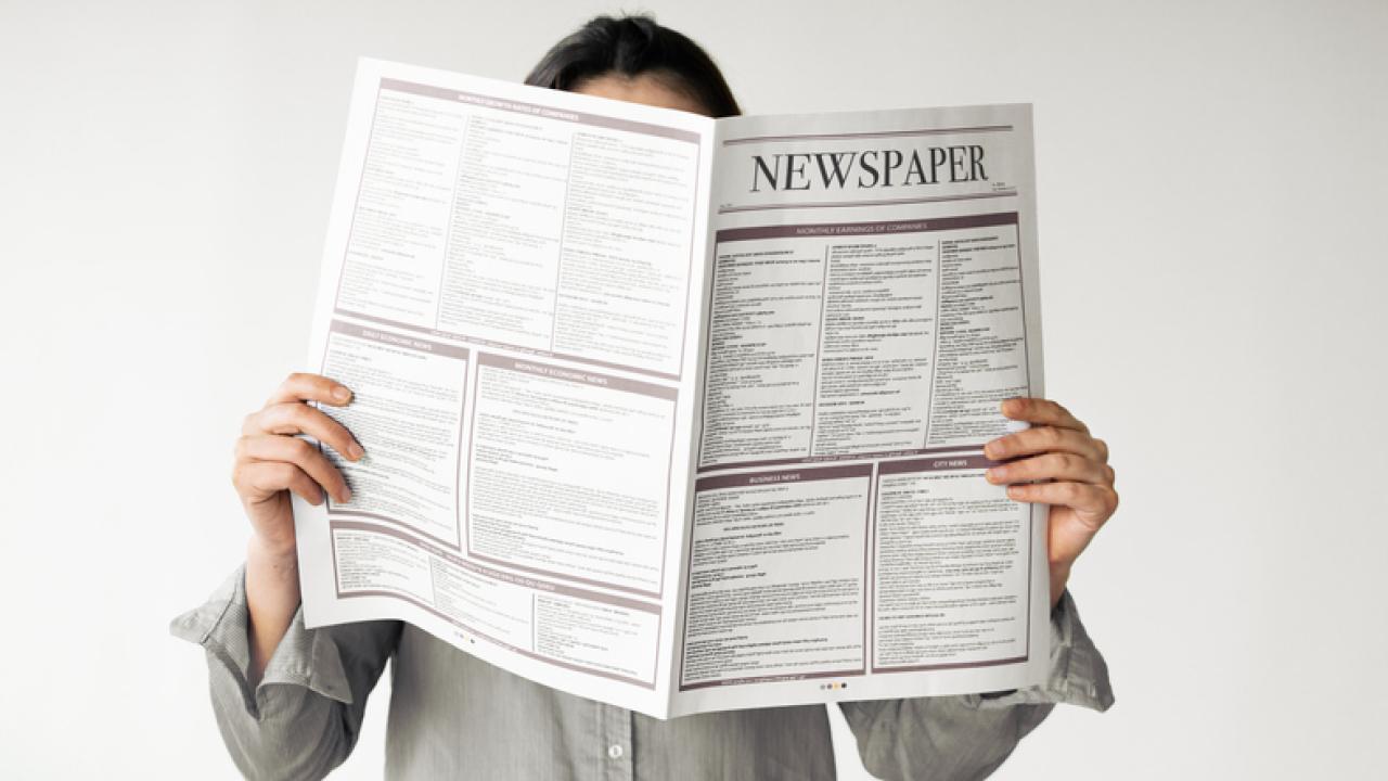 Person reading newspaper in front of their face.