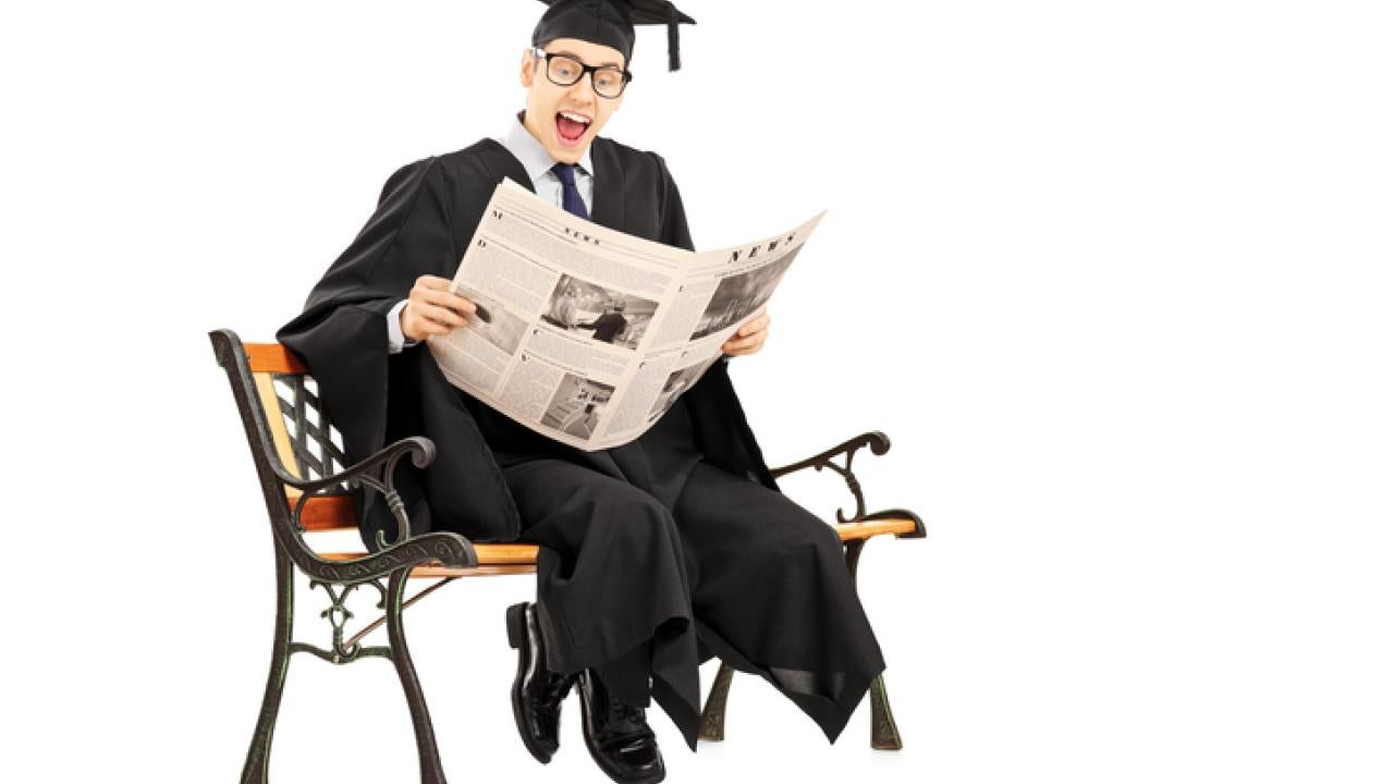 College graduate seated in a chair reading a newspaper