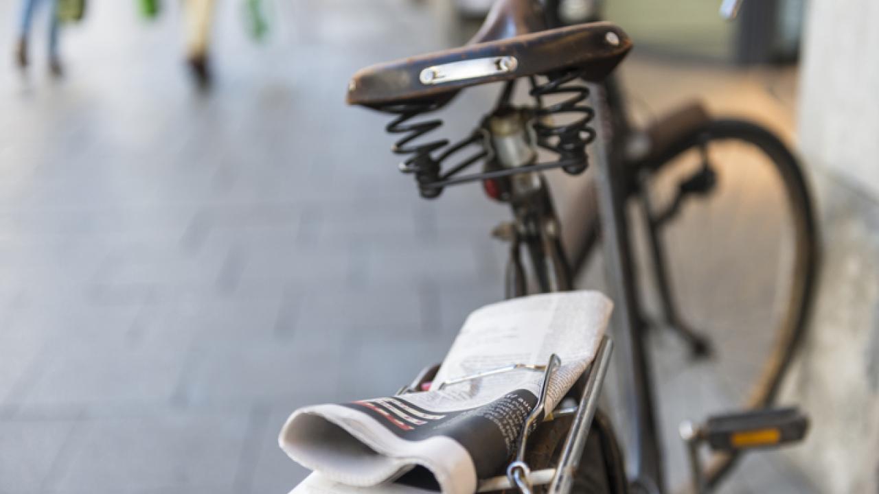 Old fashioned bike outside with a newspaper strapped to it.