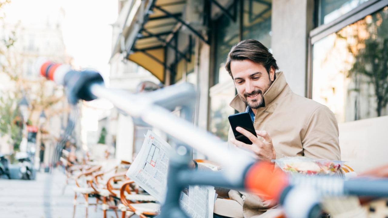 Man outside in coat with bike reading news on his phone.