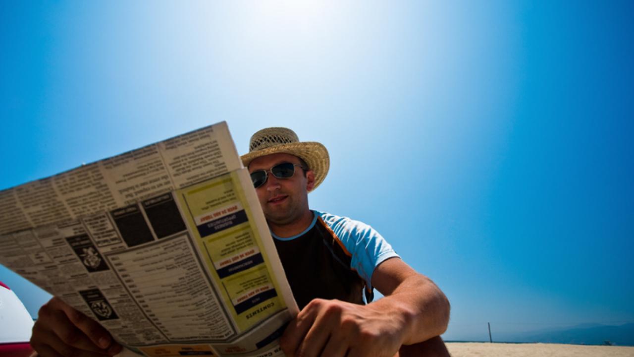 Smiling man on hat reading a paper on the beach
