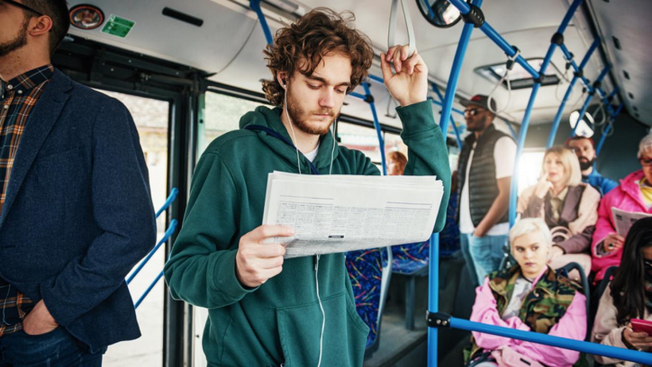 Bearded man reading a newspaper on the bus