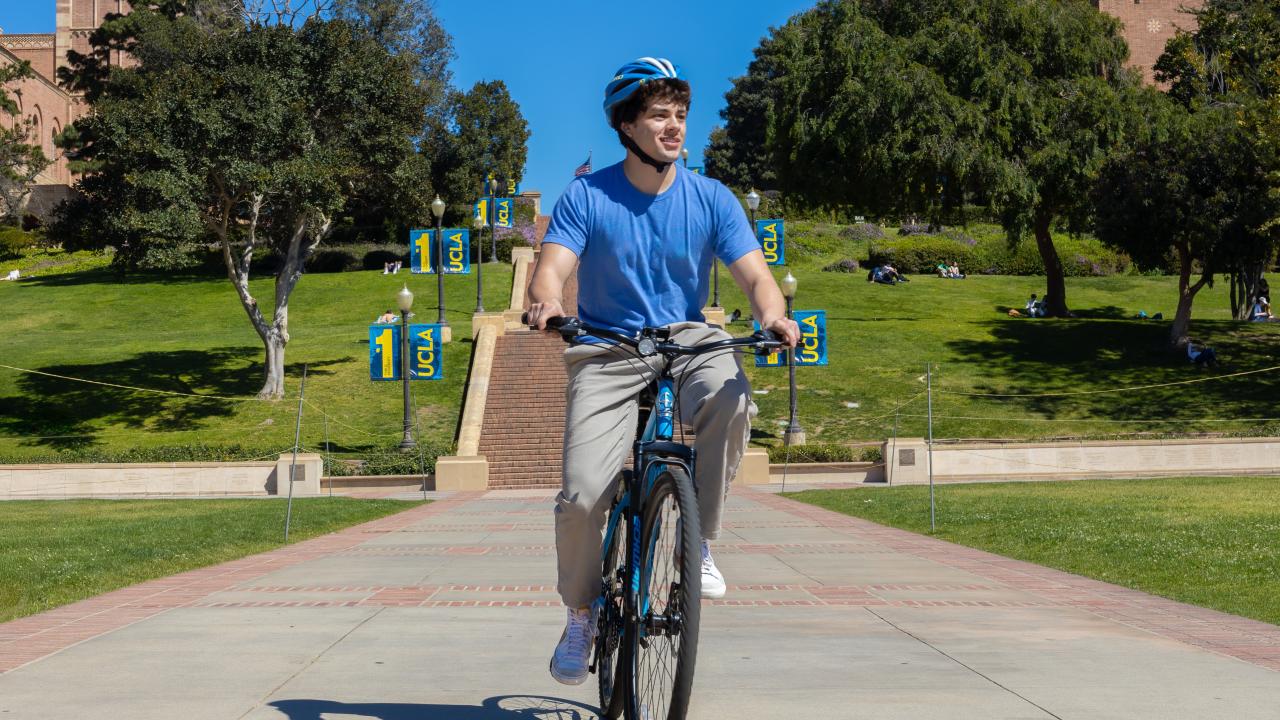 Male student riding a bike with Janss Steps in the background