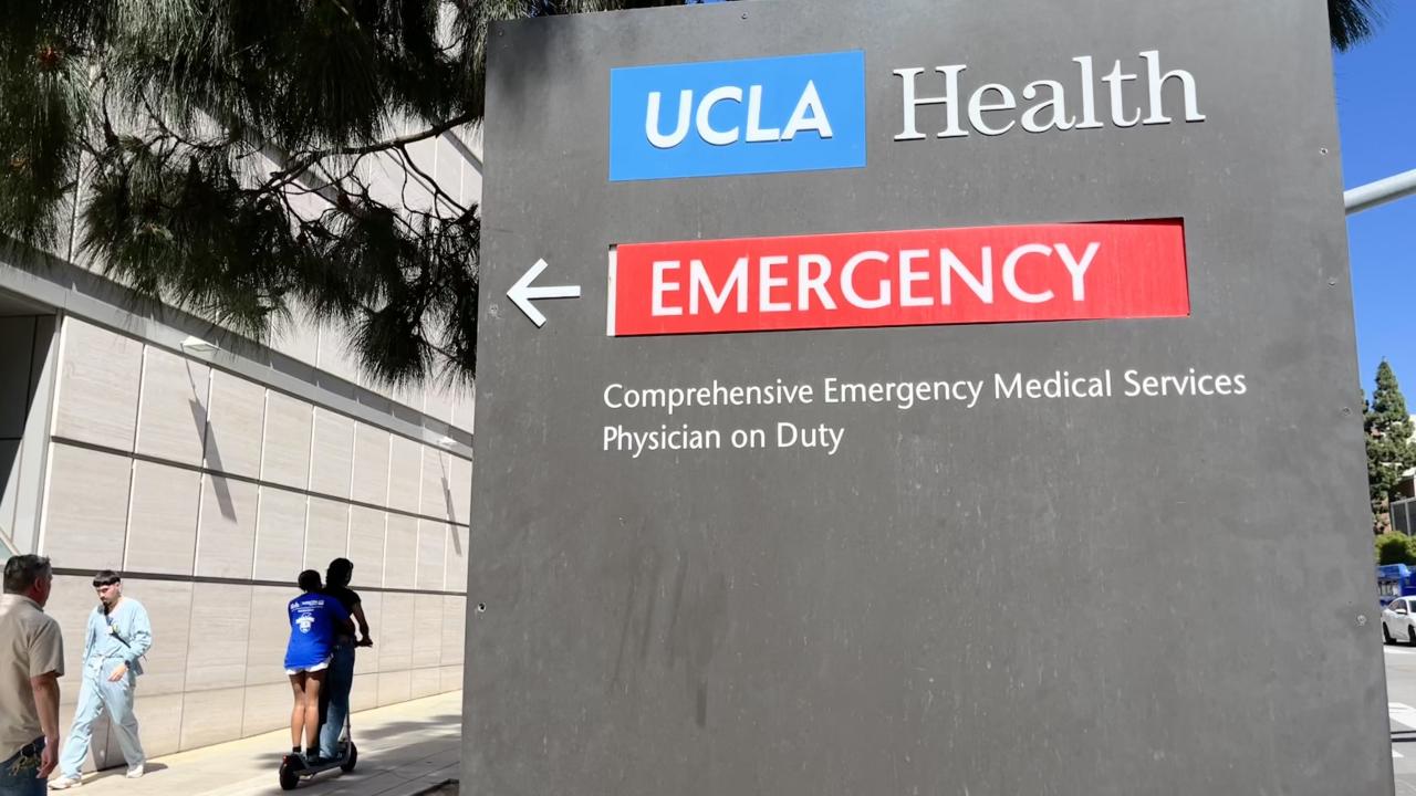 Reckless tandem scooter riders on the sidewalk near the emergency room sign