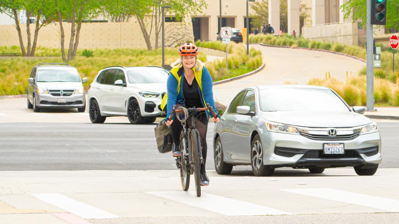 Woman on a bicycle riding on campus with a car next to her