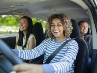 Young girl driving car with friends in passenger and back seats