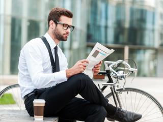 Cyclist reading the paper on a bench outside.