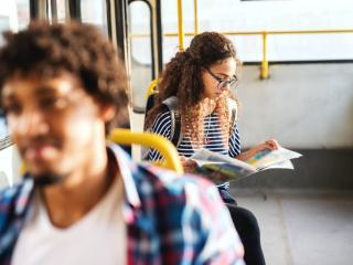 Young women reading newspaper and sitting while waiting bus to start.