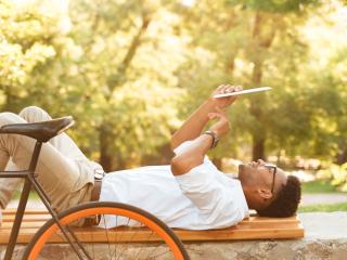 Content man on a bench next to a bike reading a newspaper.