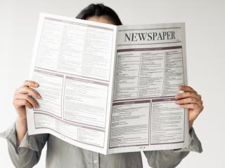 Person reading newspaper in front of their face.