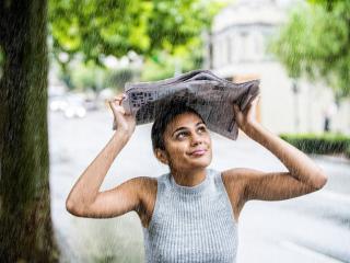 Woman outside holding newspaper over her head in the rain