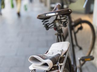Old fashioned bike outside with a newspaper strapped to it.
