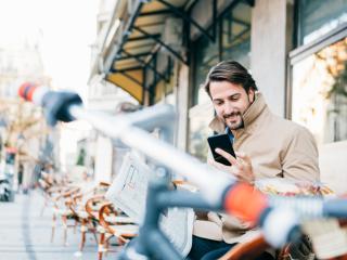 Man outside in coat with bike reading news on his phone.