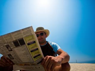 Smiling man on hat reading a paper on the beach
