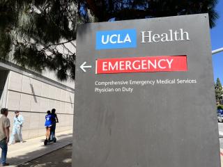 Reckless tandem scooter riders on the sidewalk near the emergency room sign