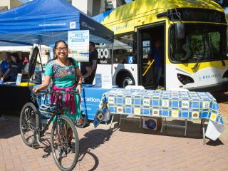 Female student with a bike at the Rideshare Fair with a BruinBus in the background