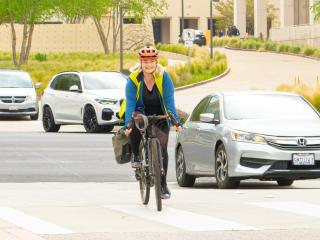 Woman on a bicycle riding on campus with a car next to her
